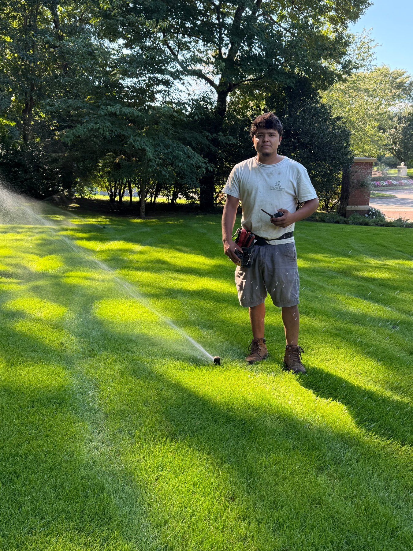 Sprinkle Smart team member standing beside a sprinkler on a green lawn